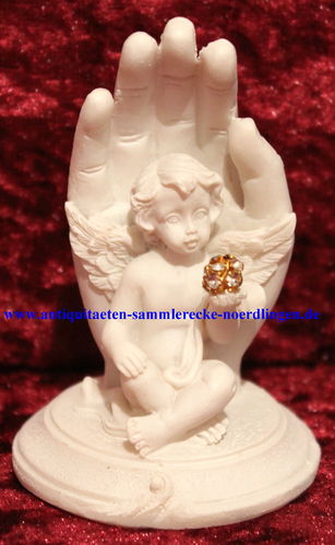 Engel auf Sockel sitzend ausgespreizten Flügel linken Hand Diamantkugel Hintergrund schützende Hand